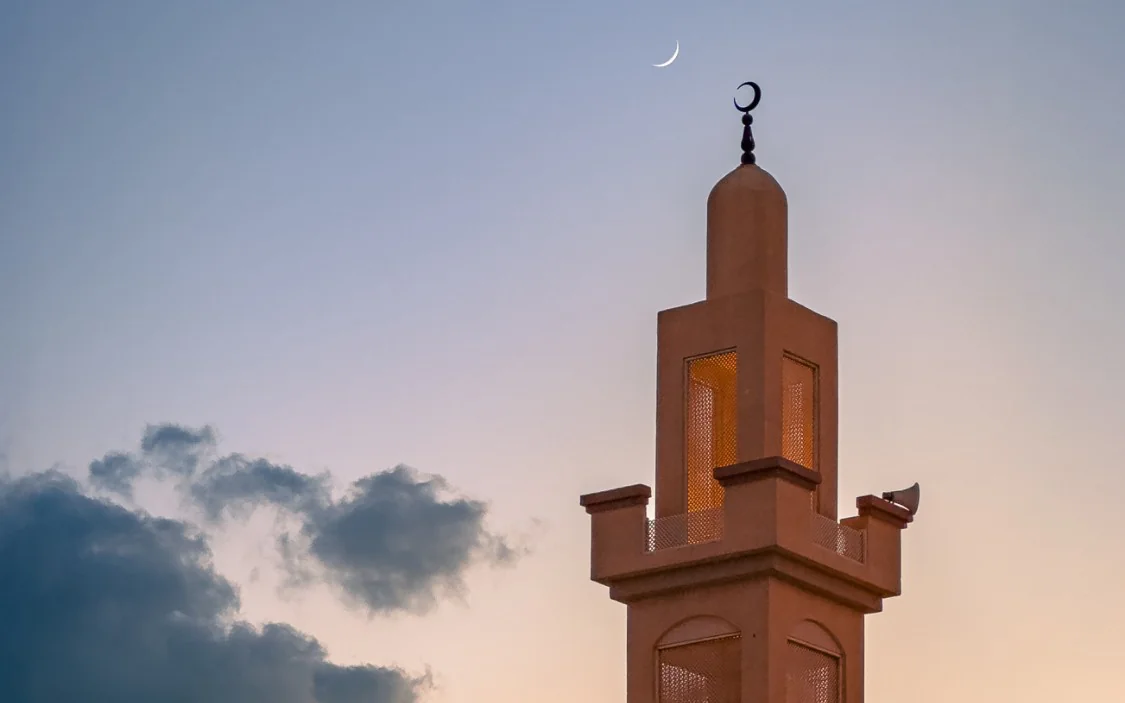 A minaret with a crescent moon in the early morning sky